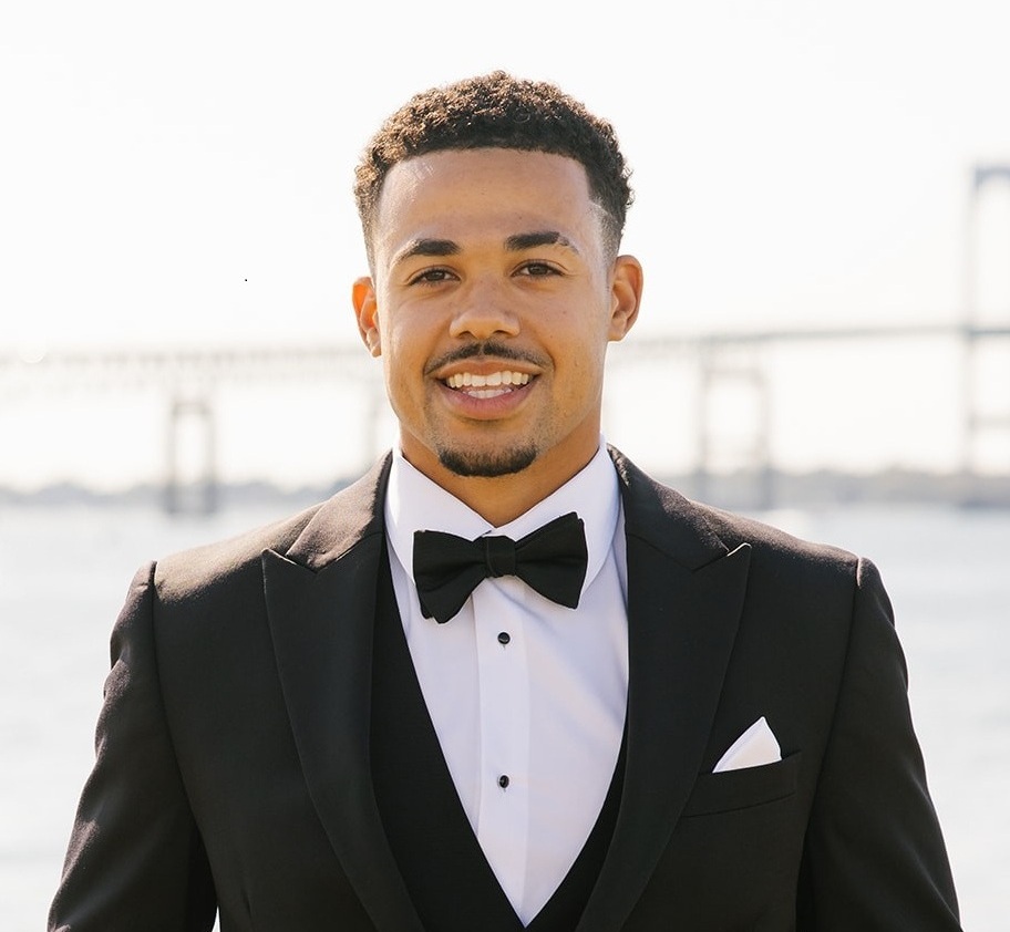 Garrett Jones in a formal black suit before a waterfront bridge